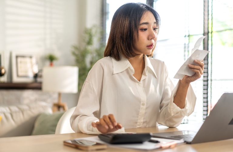 Smiling asian woman using calculator and calculate bills on laptop_s