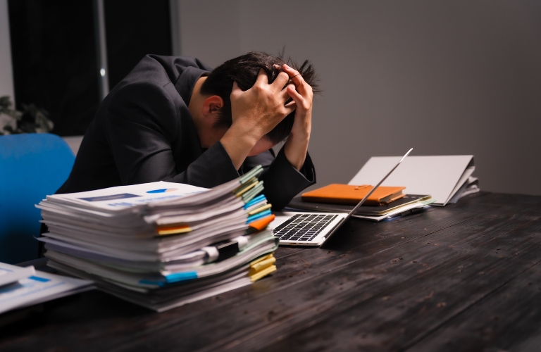 stressed young Asian man in a formal suit works late at night at his desk