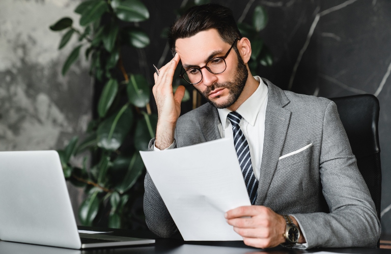 Caucasian stressed businessman checking documents while working on laptop